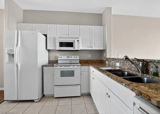 Kitchen featuring white appliances, white cabinetry, dark stone countertops, and light tile patterned flooring