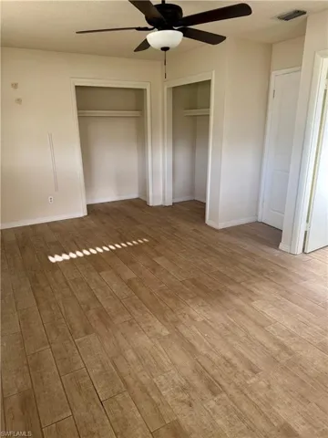 Unfurnished bedroom with multiple closets, baseboards, wood finished floors, and visible vents