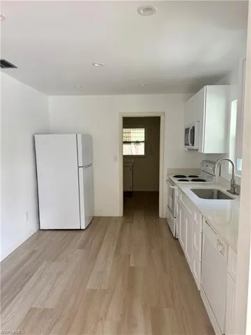 Kitchen featuring white cabinets, light wood-style flooring, a sink, visible vents, and white appliances