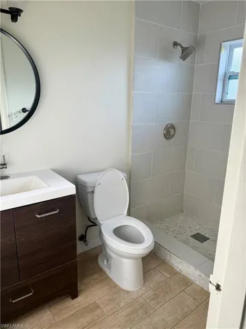 Full bath featuring a tile shower, toilet, vanity, and wood finished floors