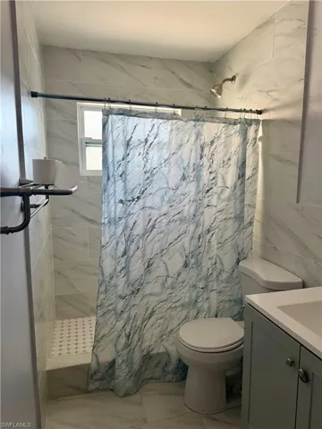 Full bath with vanity, tile walls, marble finish floor, a tile shower, and toilet