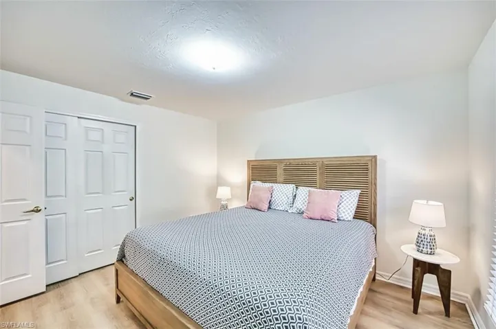 Bedroom with light wood-style floors, a textured ceiling, a closet, visible vents, and baseboards