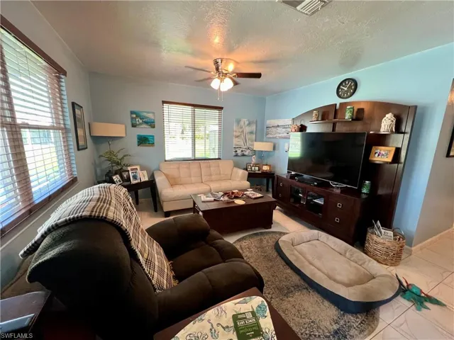 Living room with a wealth of natural light, tile patterned floors, a textured ceiling, and ceiling fan