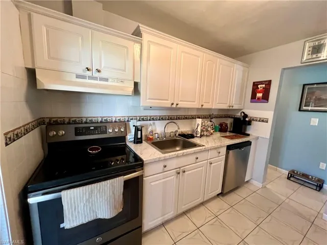 Kitchen with sink, white cabinets, decorative backsplash, and stainless steel appliances
