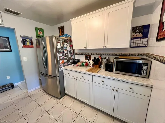 Kitchen with appliances with stainless steel finishes, white cabinetry, backsplash, and light tile patterned flooring