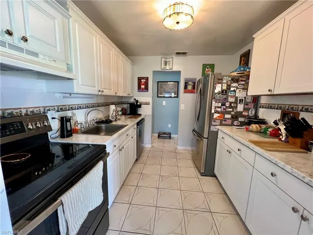 Kitchen featuring white cabinetry, tasteful backsplash, light tile patterned floors, stainless steel appliances, and sink