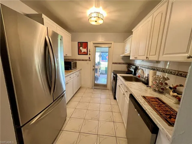 Kitchen with light tile patterned flooring, stainless steel appliances, white cabinets, decorative backsplash, and sink