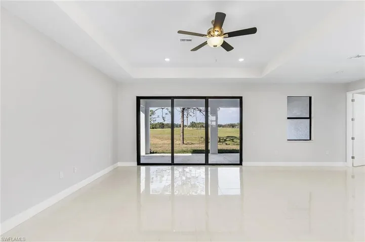 Tiled empty room with ceiling fan and a tray ceiling