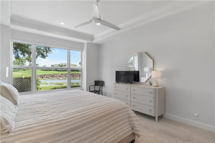 Bedroom with a tray ceiling, light colored carpet, ornamental molding, ceiling fan, and baseboards