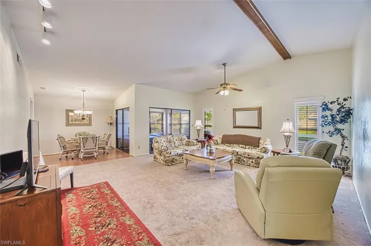 Carpeted living area with vaulted ceiling with beams, ceiling fan, healthy amount of natural light, and hanging lights