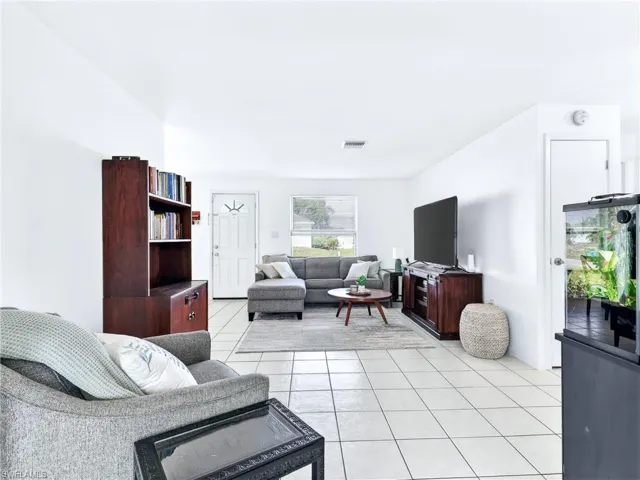 Bright living area featuring white tile flooring, a white paneled entry door with decorative glass, and a window with blinds