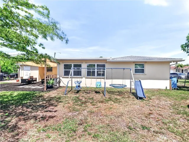 Expansive rear yard featuring a paved patio area with a sun shade, multiple windows, and a stucco exterior