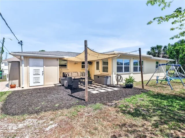 Rear exterior featuring a patio with shade sail, exterior storage shed, multiple windows, and a landscaped area with dark mulch