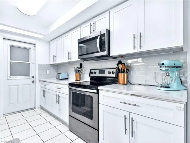 White kitchen featuring a stainless steel range and microwave, subway tile backsplash, white shaker-style cabinetry, and light-toned countertops