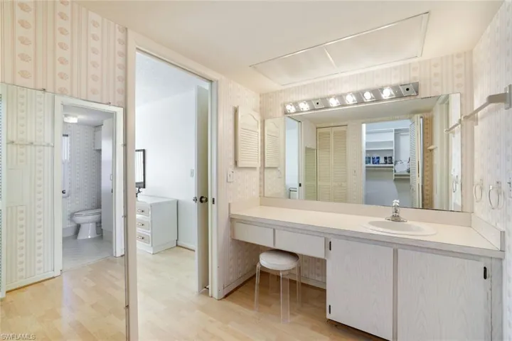 Bathroom with wallpapered walls, vanity, light wood finished floors, and a walk in closet