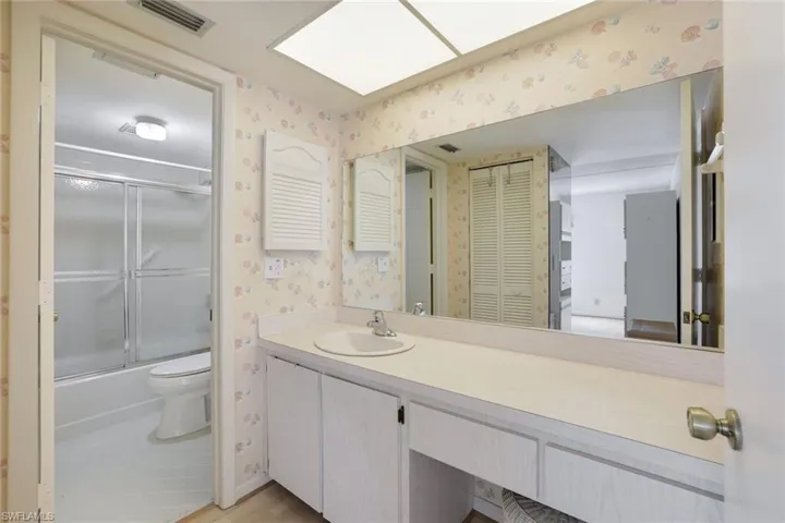 Bathroom featuring wallpapered walls, vanity, combined bath / shower with glass door, a closet, and light wood finished floors