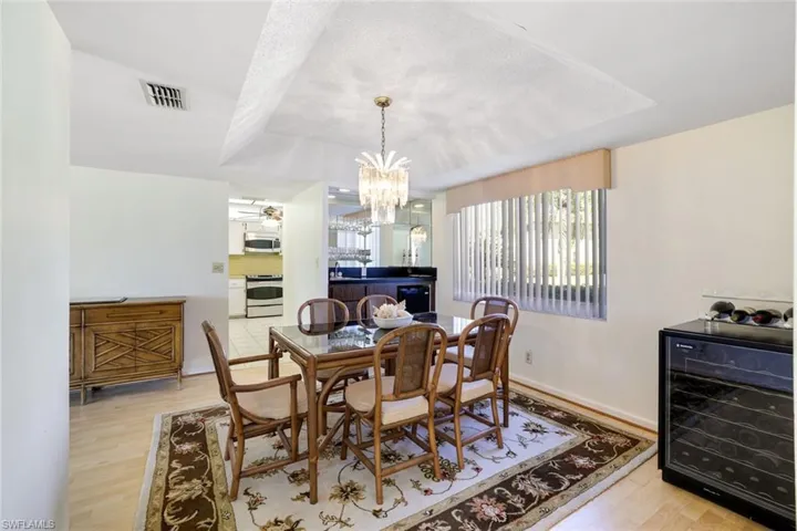 Dining space featuring wine cooler, light wood-style flooring, a chandelier, and a tray ceiling