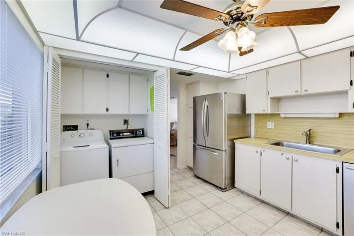 Kitchen featuring light countertops, freestanding refrigerator, white cabinetry, separate washer and dryer, and a ceiling fan
