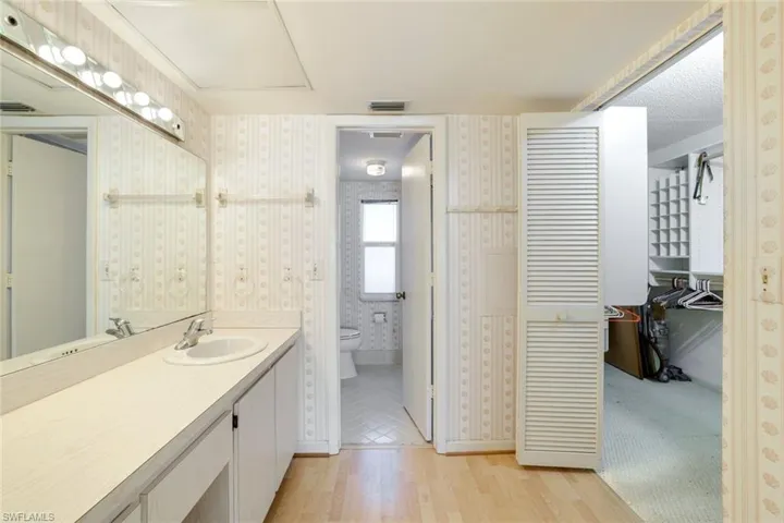 Full bath with vanity, light wood finished floors, wallpapered walls, and a closet