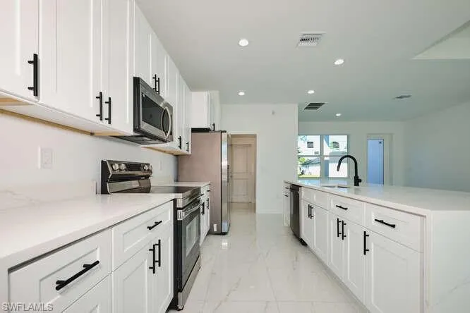 Kitchen with stainless steel appliances, white cabinetry, light marble finish flooring, recessed lighting, and an island with sink