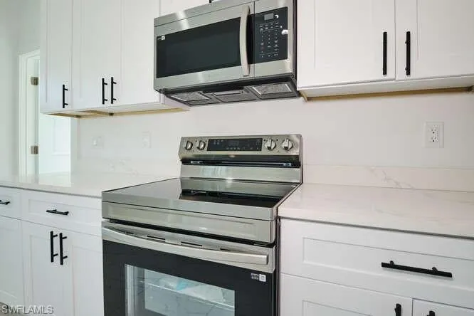Kitchen featuring stainless steel appliances, white cabinetry, and light stone counters