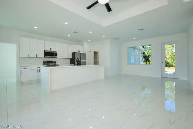 Kitchen with open floor plan, white cabinetry, an island with sink, light countertops, and stainless steel appliances