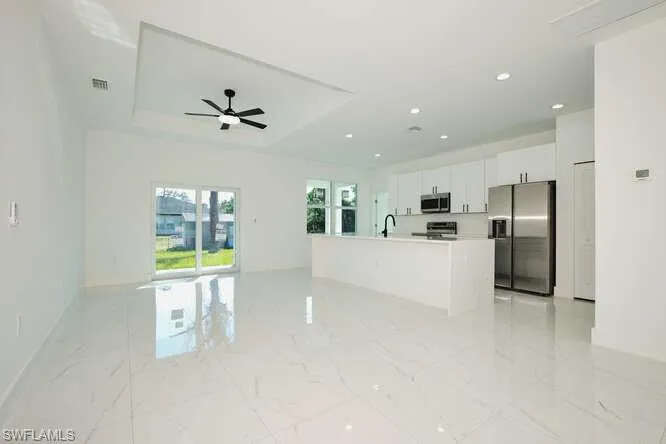 Kitchen featuring open floor plan, stainless steel appliances, white cabinetry, a kitchen island with sink, and a tray ceiling