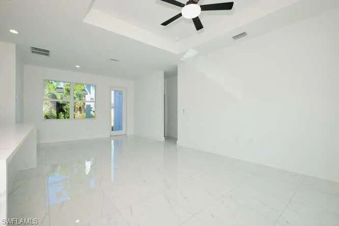 Empty room with a raised ceiling, light marble finish flooring, and ceiling fan