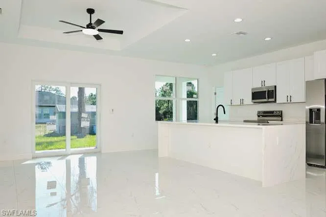 Kitchen with appliances with stainless steel finishes, white cabinets, an island with sink, light marble finish flooring, and recessed lighting