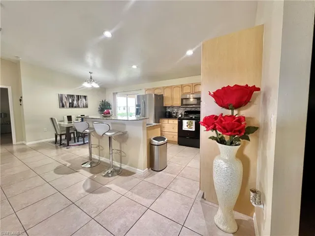 Kitchen featuring appliances with stainless steel finishes, a breakfast bar area, light tile patterned floors, light brown cabinetry, and a center island