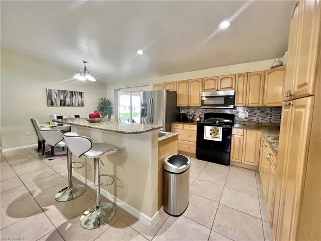 Kitchen with stainless steel appliances, hanging light fixtures, dark stone counters, backsplash, and a breakfast bar