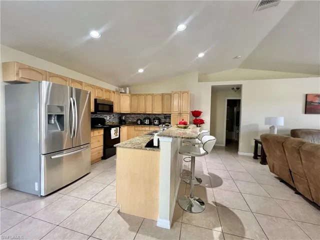 Kitchen featuring vaulted ceiling, stainless steel refrigerator with ice dispenser, light brown cabinets, dark stone countertops, and black / electric stove