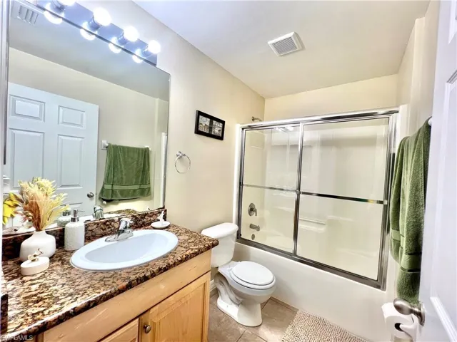Bathroom featuring vanity, enclosed tub / shower combo, and light tile patterned flooring