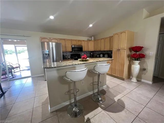 Kitchen with a breakfast bar area, stainless steel appliances, tasteful backsplash, lofted ceiling, and light tile patterned flooring