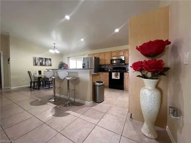 Kitchen featuring a breakfast bar, appliances with stainless steel finishes, light tile patterned floors, backsplash, and a kitchen island