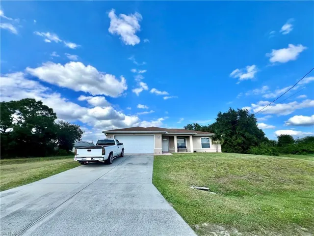 Ranch-style house with driveway, a front yard, a garage, and stucco siding