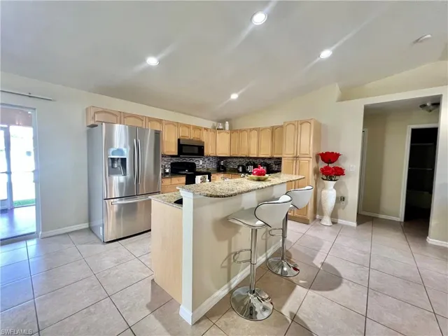 Kitchen with appliances with stainless steel finishes, vaulted ceiling, light brown cabinets, tasteful backsplash, and a breakfast bar area