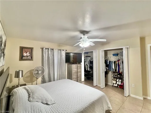 Bedroom with light tile patterned floors, multiple closets, and a ceiling fan