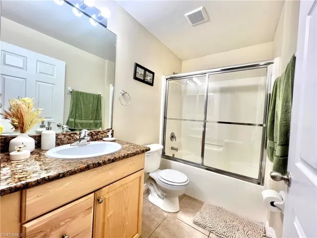 Bathroom featuring vanity, bath / shower combo with glass door, and light tile patterned flooring
