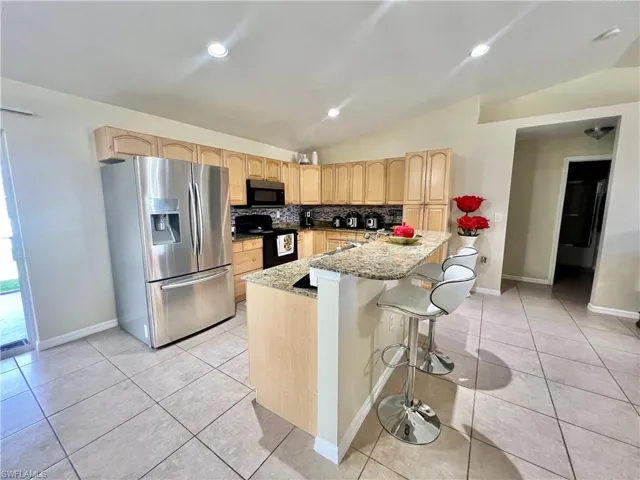 Kitchen with light brown cabinets, lofted ceiling, appliances with stainless steel finishes, a breakfast bar, and light tile patterned floors