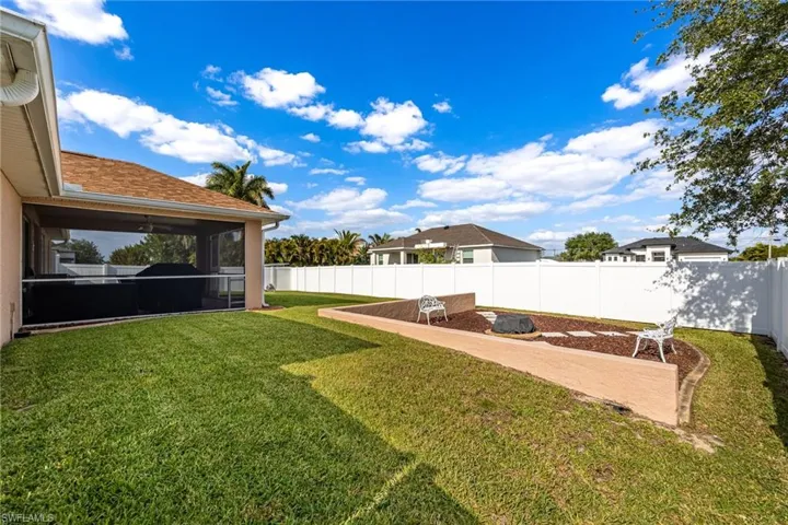 The property features a screened-in patio overlooking a spacious lawn, a decorative landscaped area with two benches, and a white privacy fence