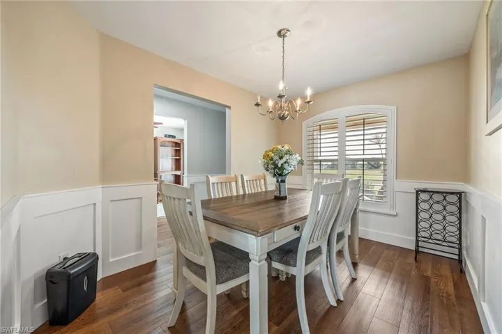 This dining area features LVP woodgrain flooring, wainscoting, an arched window with plantation shutters, and a chandelier