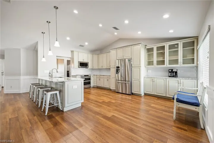 Spacious kitchen featuring LVP wood floors, pendant lighting, white cabinetry, and stainless steel appliances