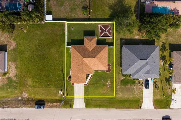 Aerial view of the property featuring a brown hip roof, a concrete driveway, and a well-maintained lawn