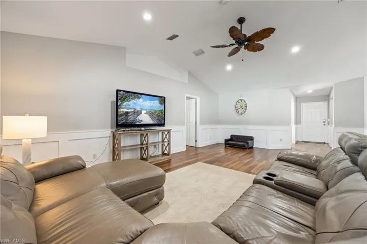 Living area featuring warm-toned LVP wood flooring, a textured area rug, and white wainscoting