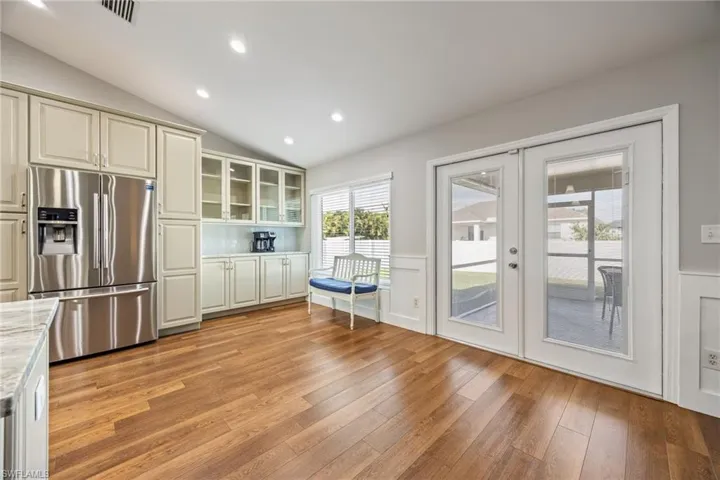 Kitchen featuring LVP wood grain floors, stainless steel refrigerator, light-colored cabinetry with some glass-front doors, recessed lighting, and French patio doors