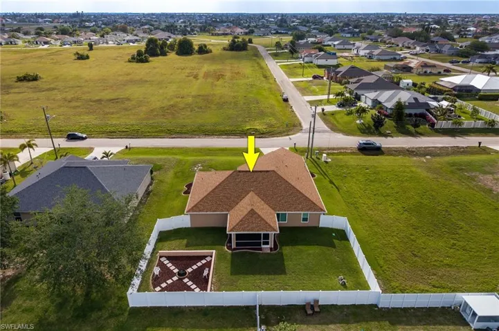 Aerial view of the property featuring a brown shingle roof, a white fence, and a green lawn