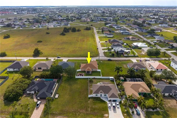 Aerial view of the property and its surrounding neighborhood, featuring a large grassy lot, paved roads, and several residential homes