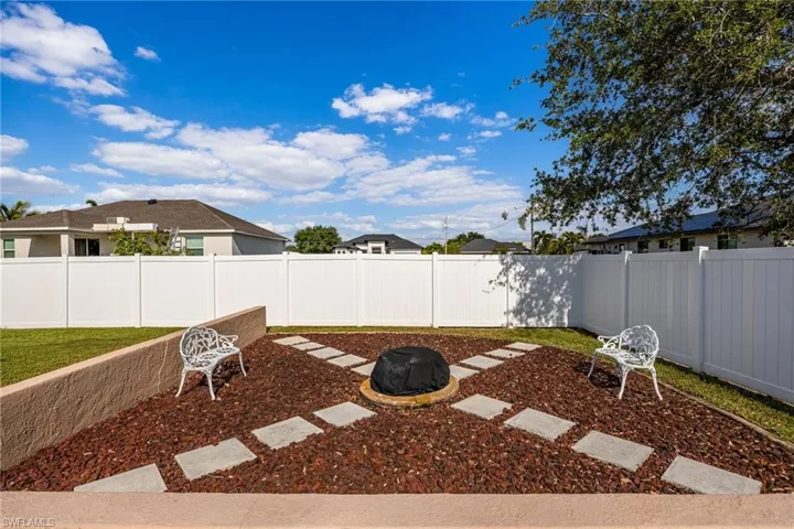 The property features a fenced backyard with a landscaped area, including a fire pit, decorative stepping stones, and two white benches with electrical outlets