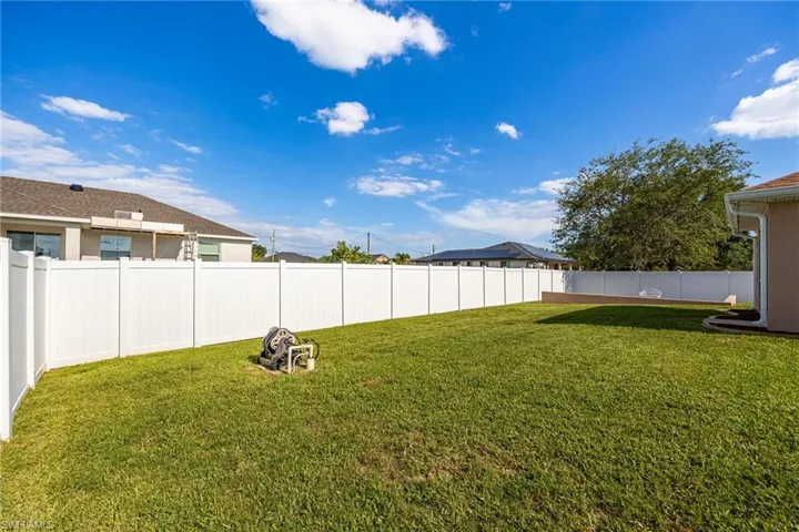 The property features an extensive, well-maintained lawn, surrounded by a tall white privacy fence, providing a secluded outdoor space